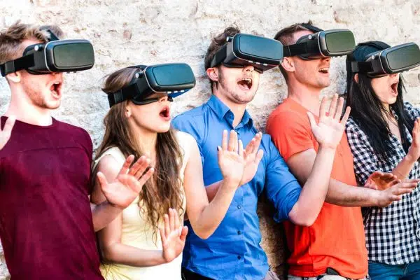 5 jovens boquiabertos e com os braços levantados em frente a uma parede usando óculos de realidade virtual